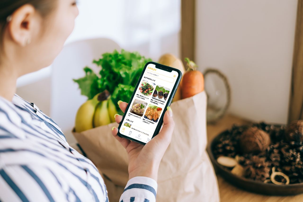 食材を背景にCOOPiiの画面を表示したスマートフォン